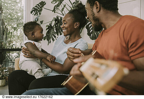 Happy mother with son sitting by father playing guitar at home