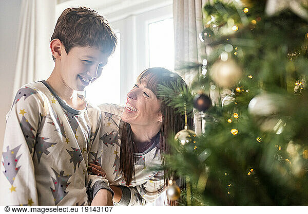 Happy mother with son standing in front of Christmas tree at home