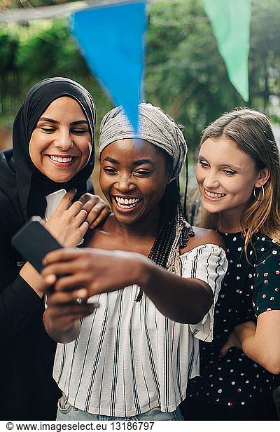 Happy multi-ethnic female friends taking selfie through smart phone in backyard