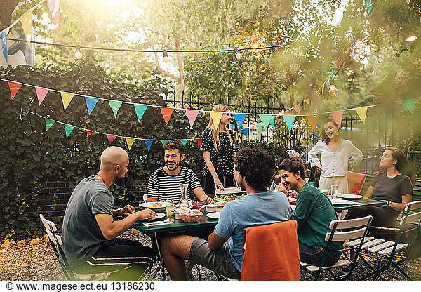 Happy multi-ethnic friends talking while having dinner during garden party
