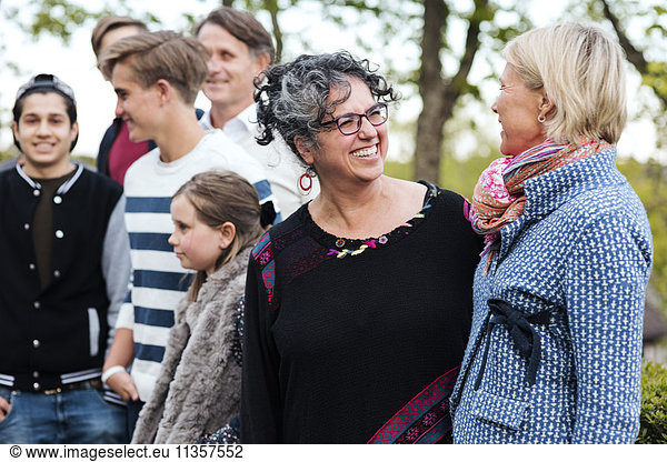 Happy multi-ethnic women talking while standing with friends and family in yard