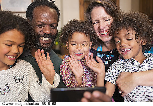Happy multiethnic family waving and video chatting with smart phone