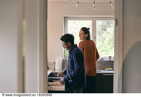 Happy multiracial couple helping each other while standing in kitchen at home