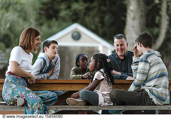 Happy multiracial family relaxing outdoors around wooden table