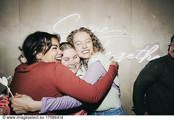 Happy multiracial female friends embracing each other in college dorm