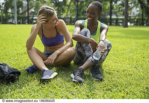 Happy multiracial friends sitting cross-legged on grass at park