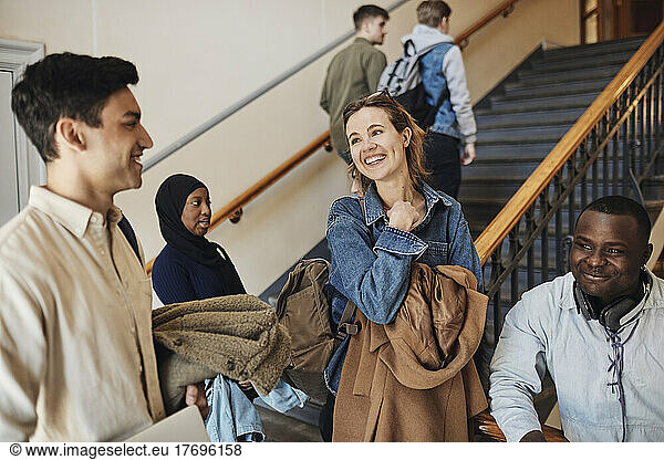 Happy multiracial friends talking to each other at staircase in university