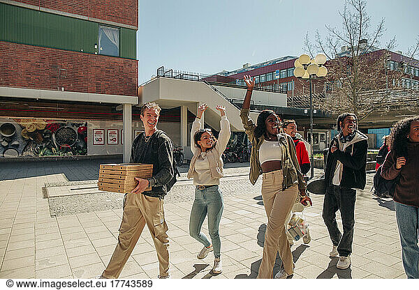 Happy multiracial friends waving hands while walking at street on sunny day