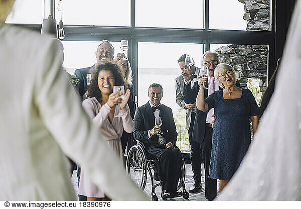 Happy multiracial guests with wineglasses cheering newlywed couple at wedding ceremony