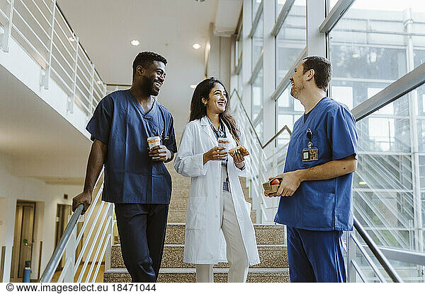 Happy multiracial healthcare workers talking while standing on staircase at hospital