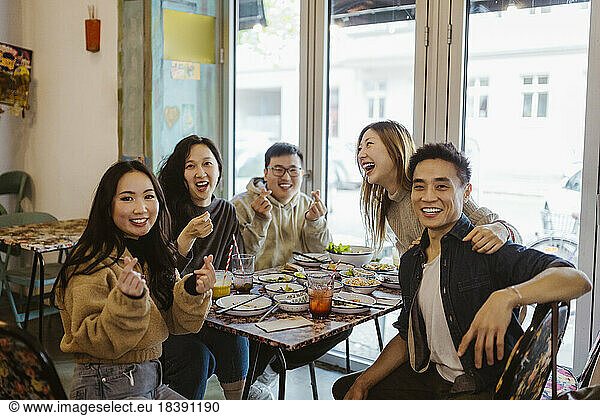 Happy multiracial male and female friends gesturing and laughing during lunch at restaurant