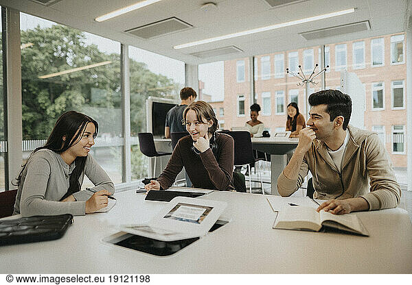 Happy multiracial male and female students studying at table in university