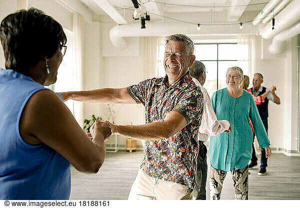 Happy multiracial senior couple dancing together in class