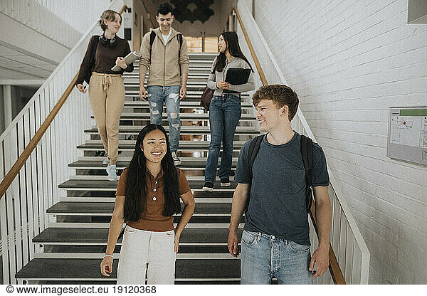 Happy multiracial students talking while moving down on steps in university