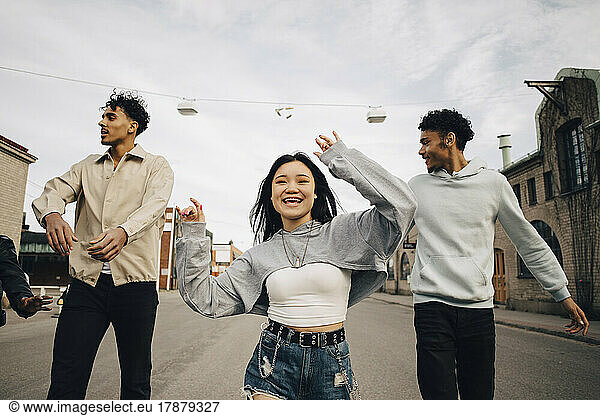 Happy multiracial young woman dancing with friends on street in city
