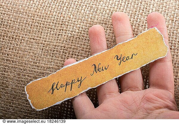 Happy new year written on a torn yellow paper in hand