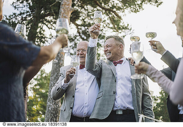 Happy newlywed gay couple raising wineglasses with family and friends at wedding
