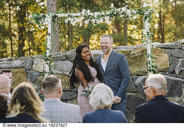 Happy newlywed multiracial couple looking at guest during wedding ceremony