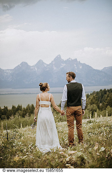 Happy newlyweds hold hands and look out at the Tetons in distance