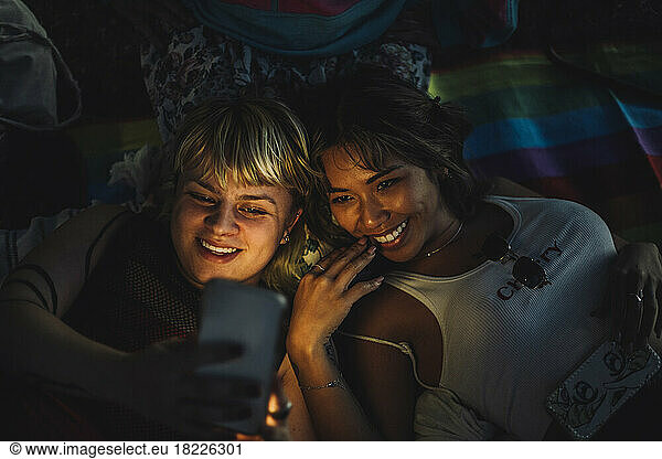 Happy non-binary person taking selfie with female friend through smart phone
