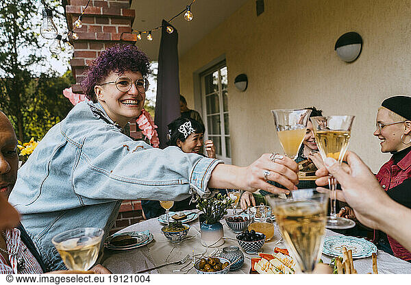 Happy non-binary person toasting drinks with friends during party in back yard