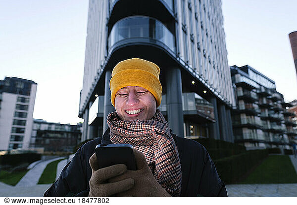 Happy non-binary person using smart phone in front of building