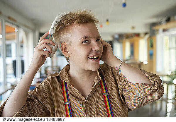Happy non-binary person wearing headphones listening to music at cafe