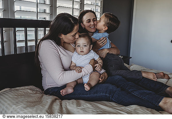 Happy non-traditional family with two moms and kids cuddling at home