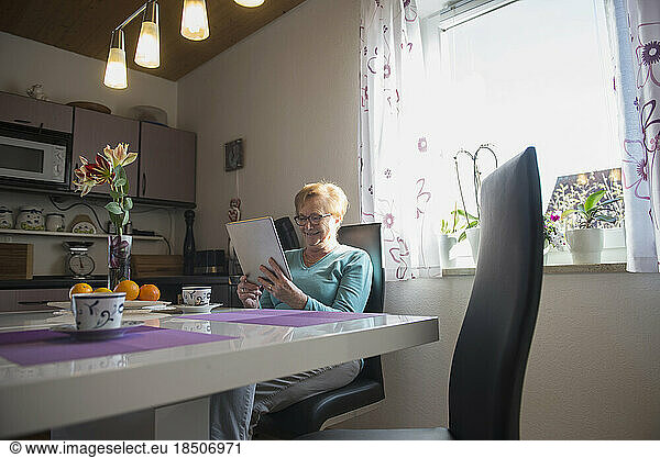 Happy old woman watching digital tablet at breakfast table
