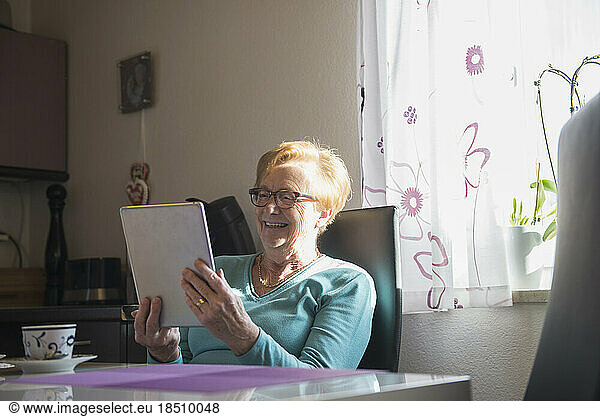 Happy old woman watching digital tablet at dining table