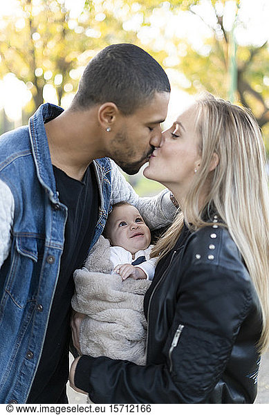 Happy parents kissing in park  with baby son between them