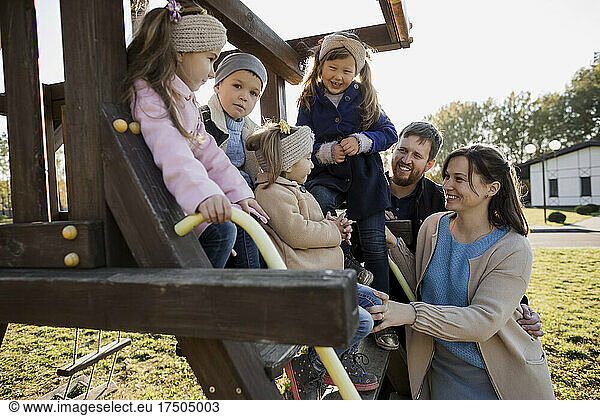 Happy parents looking at children sitting on outdoor play equipment