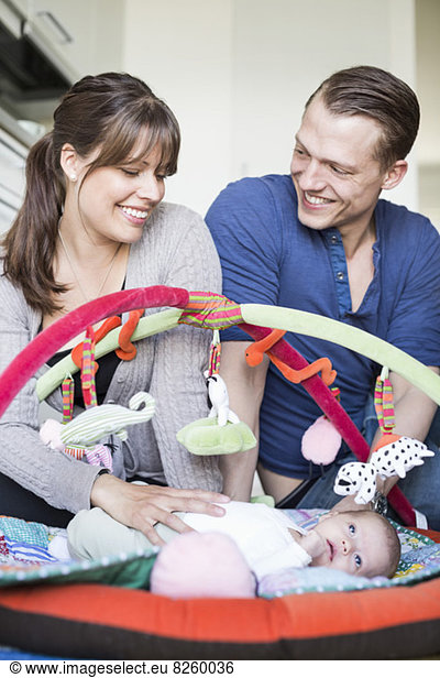 Happy parents with baby girl lying in play mat at kitchen