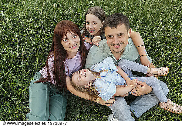 Happy parents with daughters sitting and having fun in field