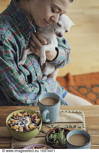 happy person cuddles cute dog at home with coffee and breakfast
