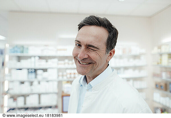 Happy pharmacist in lab coat winking at store
