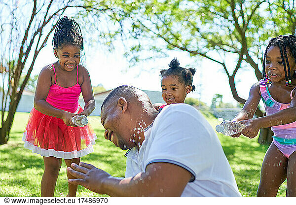 Happy playful daughters splashing father with water bottles in park