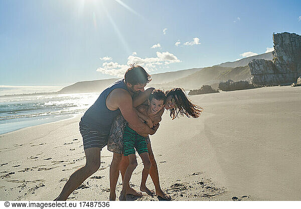 Happy playful family hugging on sunny summer beach