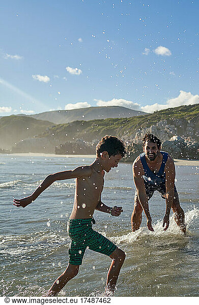 Happy playful father splashing son in sunny summer ocean