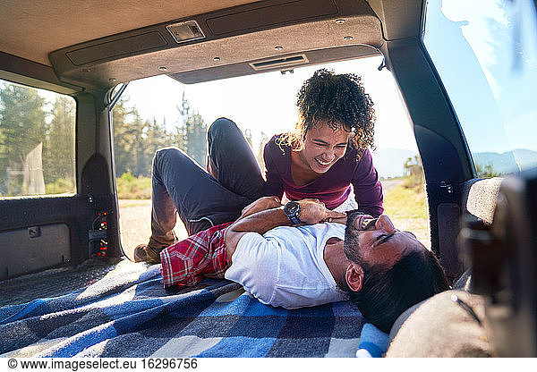 Happy playful young couple laughing on road trip at back of car