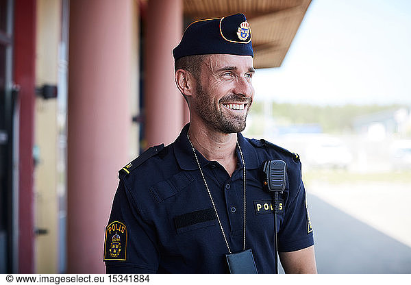 Happy policeman looking away while standing outside police station