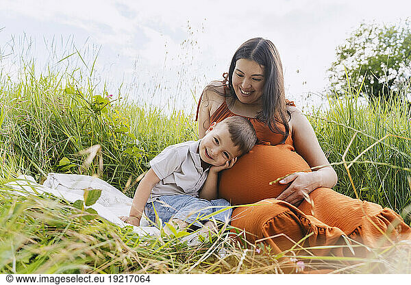 Happy pregnant mother and son spending leisure time in meadow