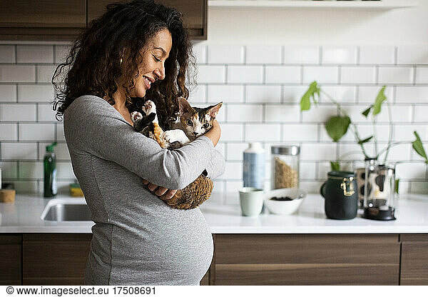 Happy pregnant woman carrying cat in kitchen