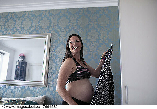 Happy pregnant woman getting dressed at bedroom closet