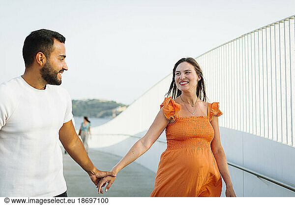Happy pregnant woman holding hand of man at footpath