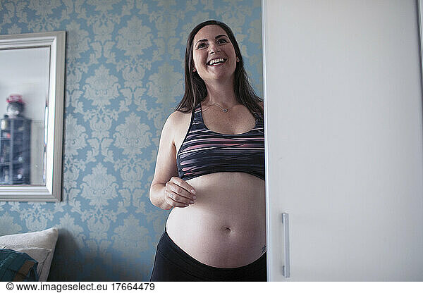 Happy pregnant woman in sports bra at bedroom closet
