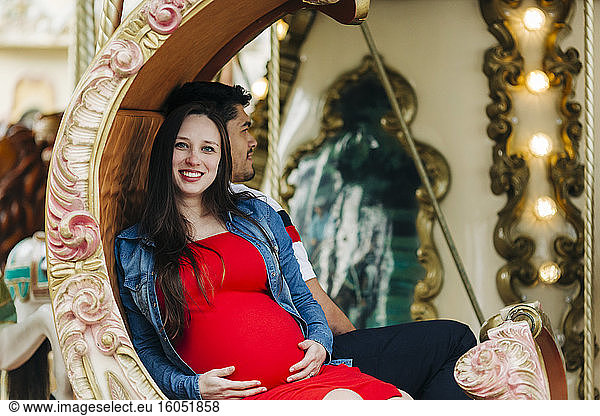 Happy pregnant woman sitting with man on carousel at amusement park  Cascais  Portugal