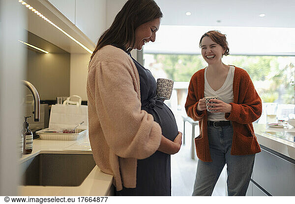 Happy pregnant woman with friend in kitchen