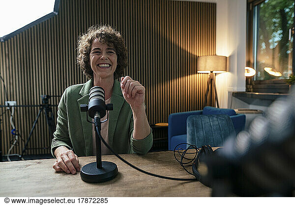 Happy presenter sitting with microphone at desk in recording studio