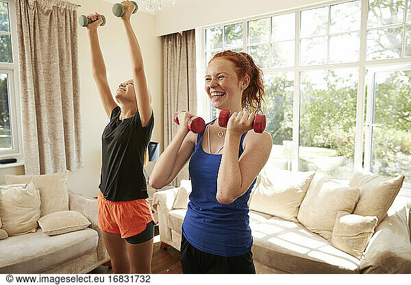 Happy preteen girl friends exercising with dumbbells in living room